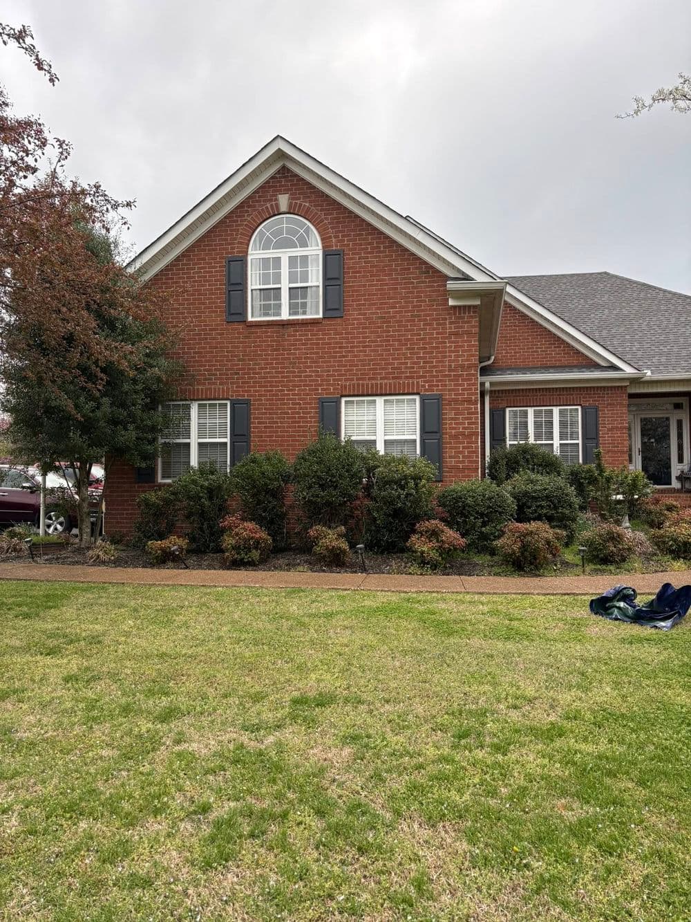 Brick house with large windows, yard, and shrubs under a cloudy sky.